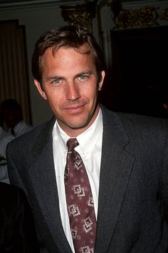 a man in a suit and tie posing for the camera with other people behind him