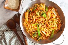 a pan filled with noodles and vegetables on top of a table next to wooden spoons