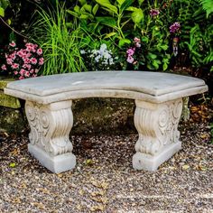 a stone bench sitting in the middle of a gravel area surrounded by plants and flowers