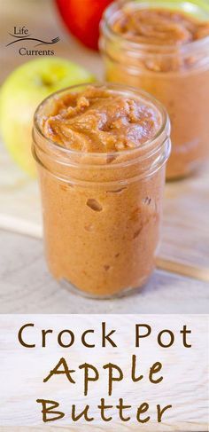 two jars filled with peanut butter sitting on top of a wooden table next to an apple