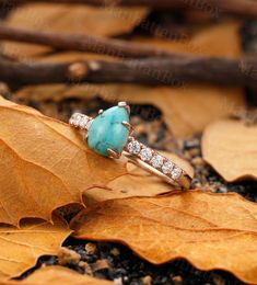 an engagement ring with a turquoise stone surrounded by brown leaves and twigs on the ground