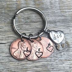 three coin keychains with the words dad and two hearts on them, sitting on top of a wooden table