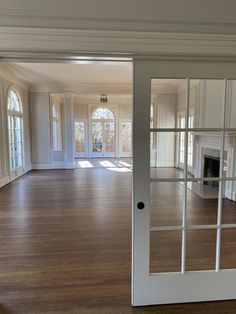 an empty living room with hard wood floors and white painted walls, large open doors leading to the dining area