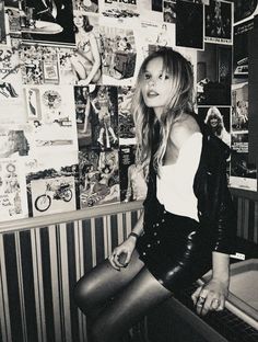 a woman sitting on top of a stool in front of a wall covered with posters