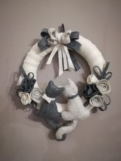 a white and gray wreath with two stuffed animals on it, hanging from the wall