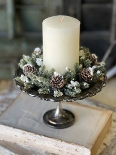 a lit candle sitting on top of a cake plate covered in pine cones and snow