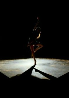 a woman is dancing in the dark with her arms spread out and legs bent forward