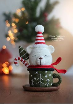 a knitted teddy bear sitting in a coffee cup with a christmas hat and scarf on