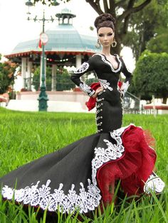 a doll is sitting in the grass wearing a black and red dress