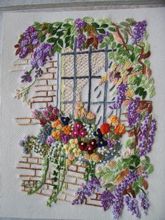 a cross stitched picture with flowers in front of a window