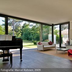 a living room filled with furniture and a piano in front of large glass doors that look out onto a yard