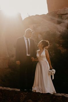 a bride and groom standing together in front of the sun