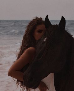 a woman is hugging a horse on the beach