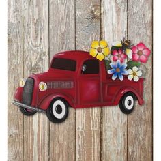 an old red truck with flowers in the bed is hanging on a wooden fence,