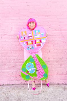 a woman in pink is holding up a heart shaped paper cutout with buildings on it