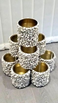 a stack of cups made out of rocks and gold rimmed tins sitting on the floor