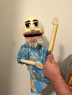 a man holding a large wooden stick with a face on it and wearing a blue shirt