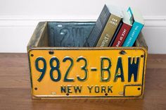 a yellow license plate holder with books in it on a wooden table next to a white wall