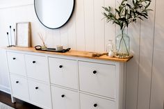 a white dresser topped with lots of drawers next to a vase filled with green plants