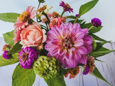 a vase filled with pink and purple flowers on top of a wooden table next to green leaves