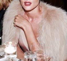 a woman sitting at a table wearing a fur coat