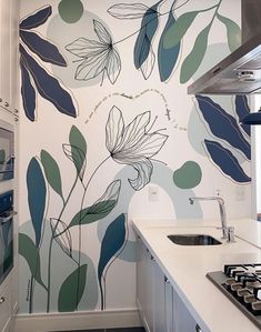 a kitchen area with a stove top oven next to a wall painted with blue and green leaves