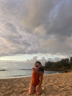 a woman sitting on top of a sandy beach next to the ocean holding a cell phone up to her ear