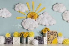 a table topped with vases filled with yellow and white flowers next to paper clouds