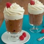 two dessert cups with whipped cream and raspberries in them on a blue place mat