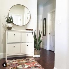 a white dresser sitting next to a mirror on top of a wooden floor with a potted plant