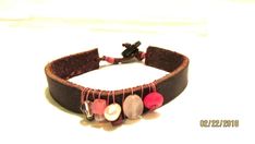 a brown leather bracelet with red and white beaded beads on the end, sitting on top of a white surface