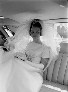 a woman sitting in the back seat of a car wearing a wedding dress and veil