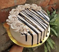 a white cake with black and gold icing on a platter next to a brick wall