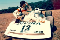 a man sitting on top of a white race car in the middle of a field