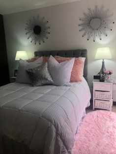 a bed with pink and silver pillows on top of it next to two nightstands