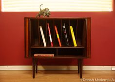 a book shelf with books on top of it in front of a red painted wall