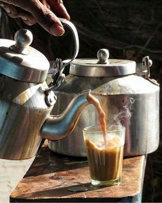 a person pours coffee into a teapot on a table with a glass next to it