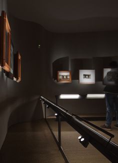 a man standing next to a railing in front of some framed pictures on the wall