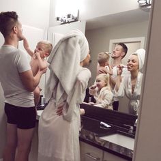 a group of people standing in front of a bathroom mirror brushing their teeth and looking at each other