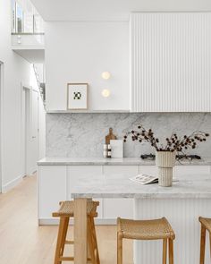 a white kitchen with marble counter tops and stools