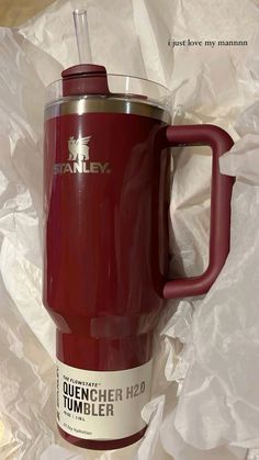 a red travel mug sitting on top of white plastic wrapper next to a straw