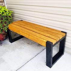 a wooden bench sitting on top of a cement floor next to a plant potted in front of a house