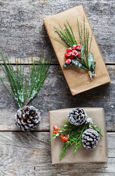 two presents wrapped in brown paper and decorated with pine cones, evergreen needles and red berries