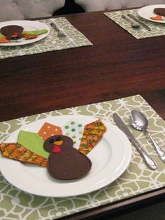 a table set for thanksgiving dinner with turkey decorations on plates and silverware in front of it