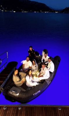 a group of people sitting on the back of a boat in the water at night