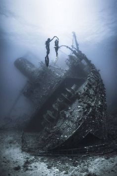 two scuba divers standing on the bottom of an old ship in the ocean under water