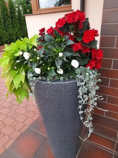 red and white flowers are in a large planter on the side of a house