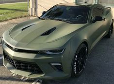 a green camo car is parked in the parking lot next to a fence and building