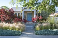 a blue door in front of a house surrounded by trees and plants on a sunny day