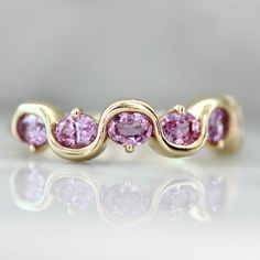 Why I Love It: This delectable morsel contains five generous helpings of the most perfectly pink oval cut sapphires. Waves of gold separate them with pops of prong details. Served in your choice of golds for the perfect treat yourself band. The Details: Available in 14k Yellow Gold, 14k White Gold, 14k Rose Gold 1.75 Carats Total Pink Oval Cut Sapphires Band Width is Approx. 1.75 mm at smallest point, and 4.95 mm at widest Band Height us Approx. 2.80 mm Made to order in your size, please allow a Pink Oval Ring, Pink Diamond Wedding Band, Pink Wedding Band, Gem Breakfast, Oval Sapphire Ring, Gold Sapphire Ring, Sapphire Band, Pink Sapphire Ring, Ringe Gold